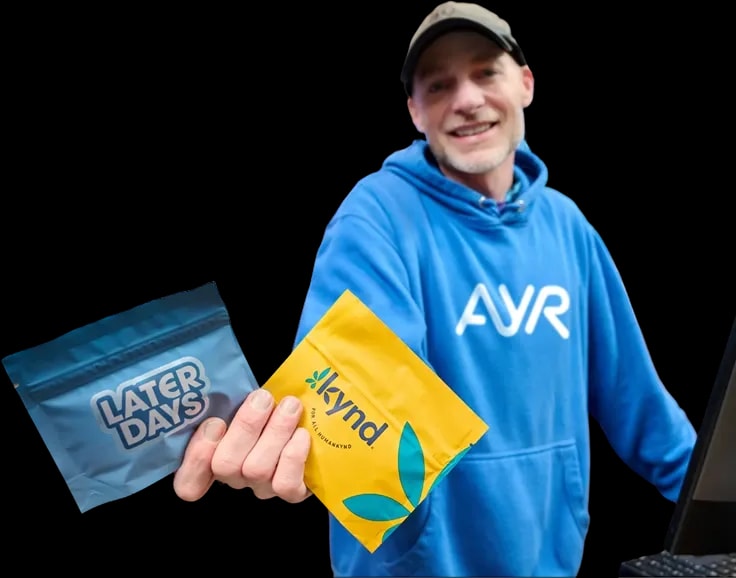 Ayr Budtender in a blue AYR hoodie holding Later Days and kynd product pouches